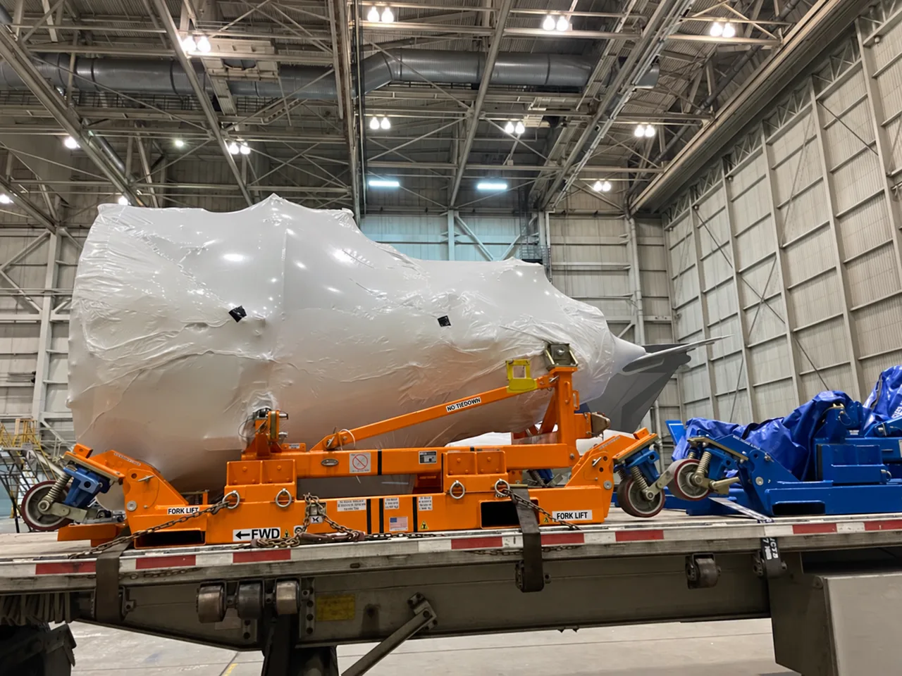 Wrapped jet engine on an orange transport stand on a trailer inside a hangar